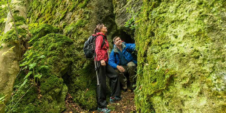 Zwei Wanderer am Eingang einer Steinhöhle auf dem Schneifelpfad im Naturpark Nordeifel Eifel